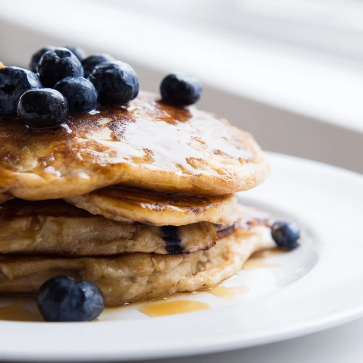 Stacks of golden brown banana pancakes with fresh berries and maple syrup drizzle on a plate.  