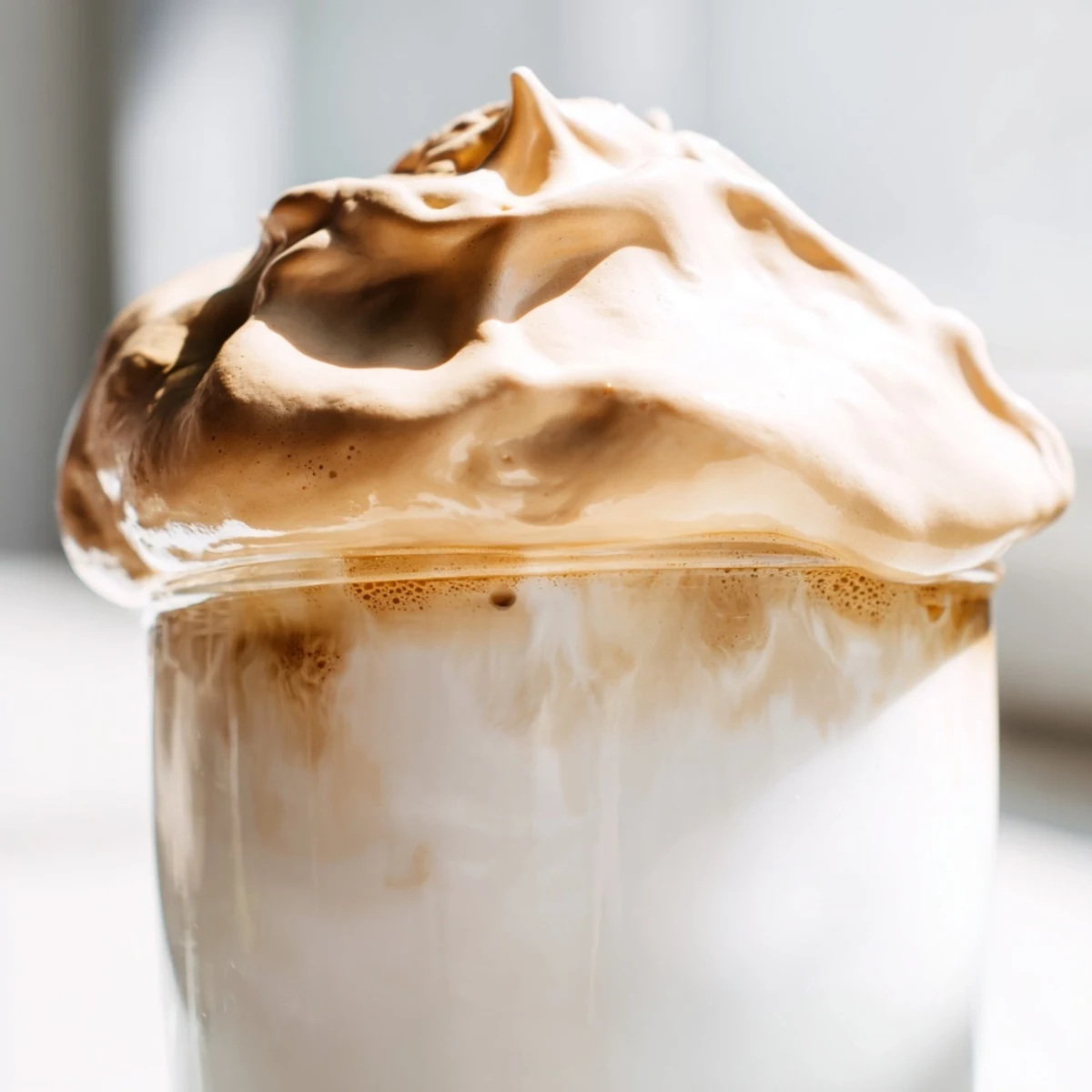 Thick, caramel-colored whipped Dalgona coffee floats atop cold milk filled with ice cubes.
