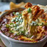 Freshly baked Buffalo Chicken Dip in a white dish, garnished with green onions and paired with sturdy tortilla chips for scooping.  
