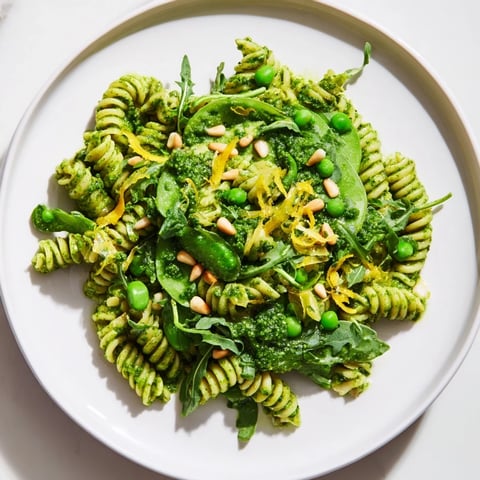 A vibrant bowl of Spring Green Pesto Pasta Salad, featuring twirled fusilli coated in basil pesto with sweet peas and peppery arugula.  
