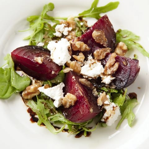 Close-up of Roasted Beet Goat Cheese Salad drizzled with balsamic vinaigrette, finished with fresh chives on a rustic plate.