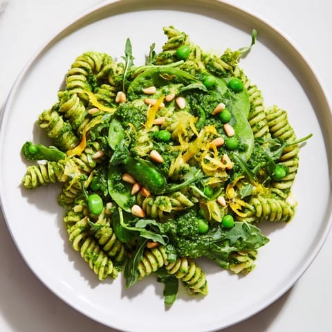 A vibrant bowl of Spring Green Pesto Pasta Salad, featuring twirled fusilli coated in basil pesto with sweet peas and peppery arugula.  