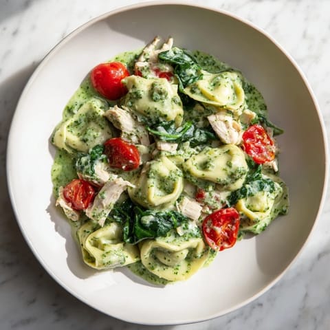 Creamy pesto tortellini skillet with rotisserie chicken, baby spinach, and halved cherry tomatoes in a bubbly sauce.  