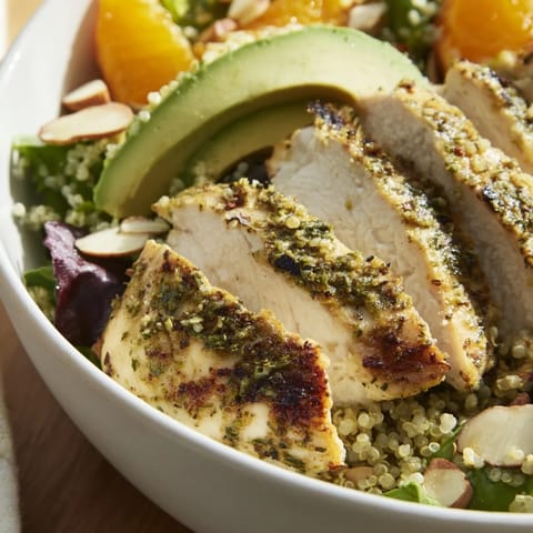 Grilled herb-marinated chicken slices over mixed greens, quinoa, and bright orange segments on a rustic wooden table.  