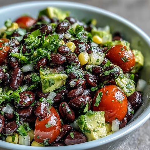 Colorful, ready-to-eat Black Bean and Veggie Bowl garnished with pumpkin seeds and lime wedges on a rustic wooden table.  