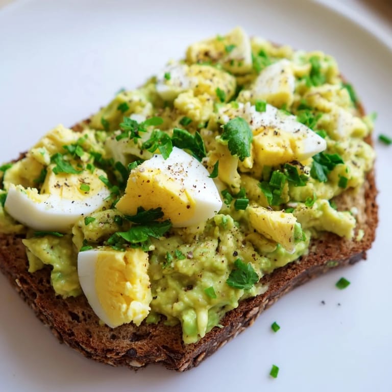 Close-up of avocado egg smash before serving, with fresh herbs and a squeeze of lemon.