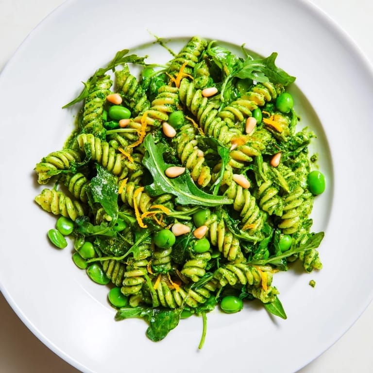 Spring Green Pesto Pasta Salad served chilled, showcasing toasted pine nuts, bright lemon zest, and crumbled feta on a rustic picnic table.  