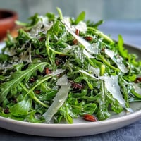 A vibrant arugula salad with tangy lemon vinaigrette and delicate Parmesan shavings, offering a fresh and peppery bite.