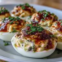 Classic Deviled Eggs with Paprika and Chives on a white platter, creamy yolk filling piped into egg whites and dusted with bright red paprika and fresh green chives.